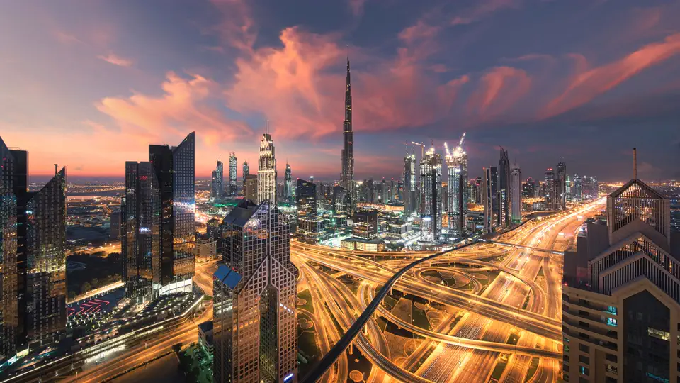 Downtown Dubai and the Burj Khalifa at dusk, with traffic light trails glowing across a Sheikh Zayed Road interchange