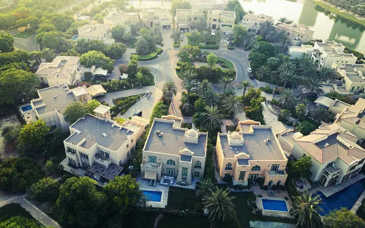 Aerial view of a Dubai villa community with private pools and palm trees in the morning light